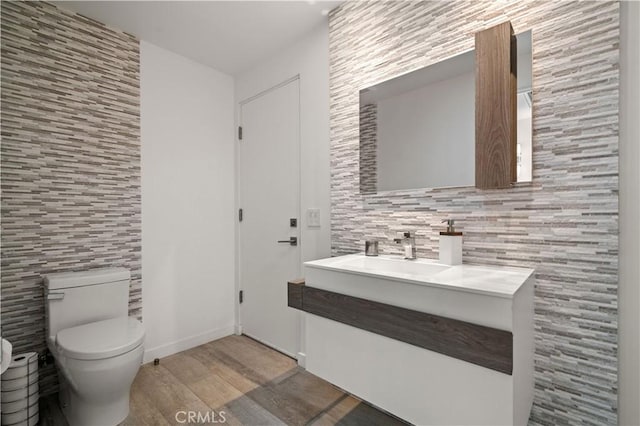 half bathroom with vanity, wood finished floors, baseboards, tile walls, and toilet