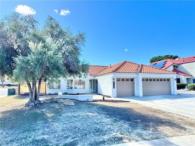 mediterranean / spanish house featuring a garage, concrete driveway, stucco siding, and a tiled roof