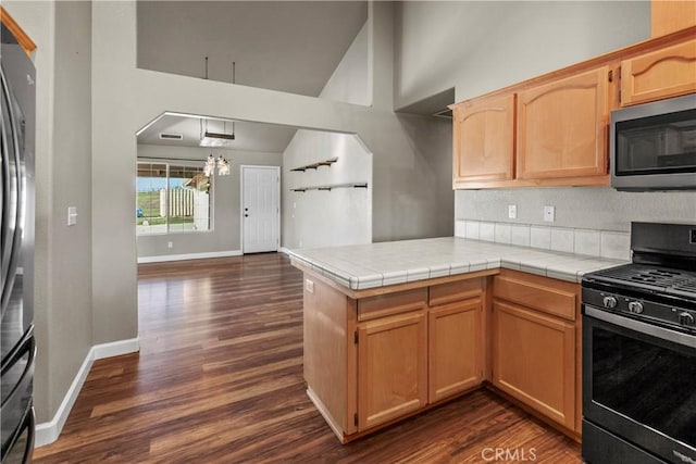 kitchen with dark wood finished floors, vaulted ceiling, a peninsula, and stainless steel appliances