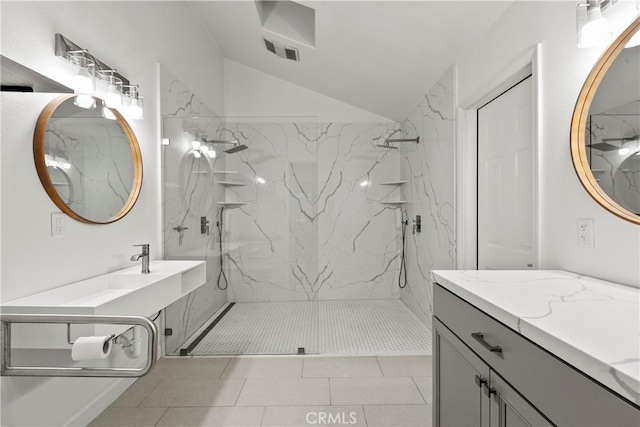 full bath with a marble finish shower, visible vents, two vanities, and vaulted ceiling