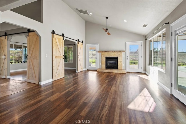 unfurnished living room featuring a barn door, wood finished floors, visible vents, and baseboards