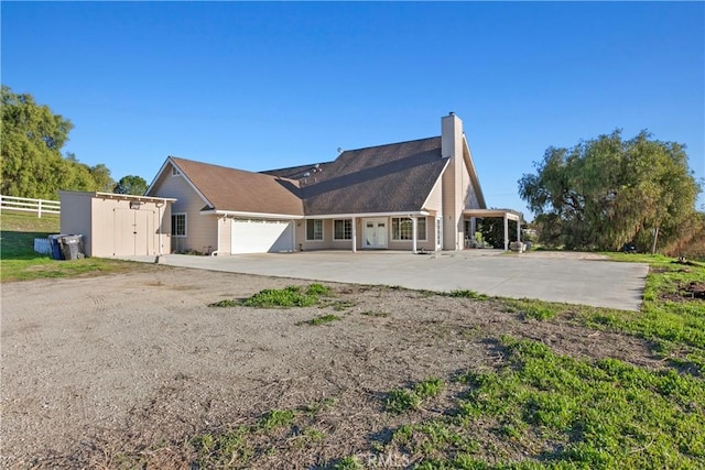 back of property with a garage, concrete driveway, a chimney, and fence