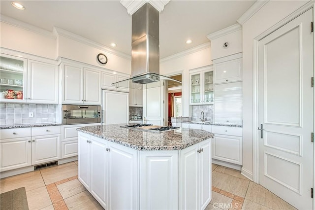 kitchen featuring a kitchen island, glass insert cabinets, decorative backsplash, island exhaust hood, and stainless steel gas stovetop