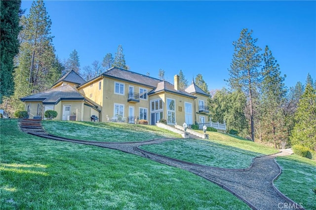 rear view of house with a yard, a chimney, and stucco siding