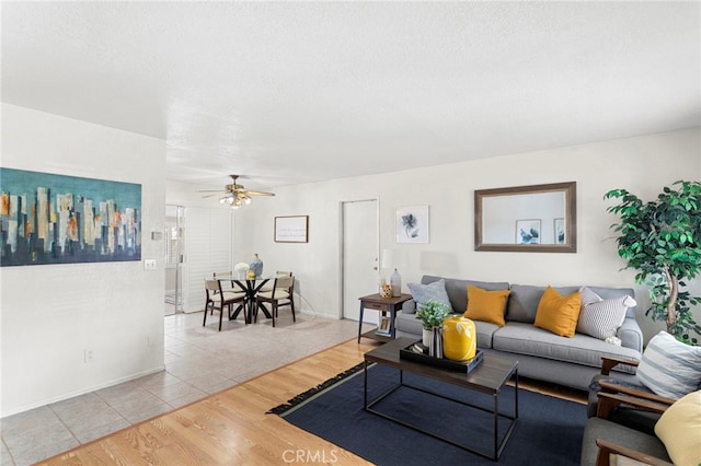 living area with light wood-type flooring, baseboards, a textured ceiling, and a ceiling fan