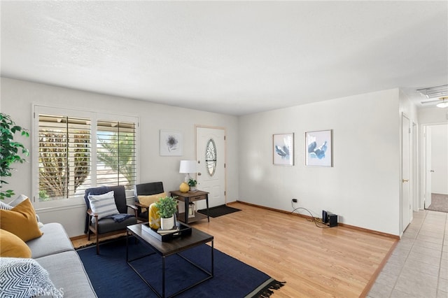 living room with light wood-type flooring, visible vents, a textured ceiling, baseboards, and attic access