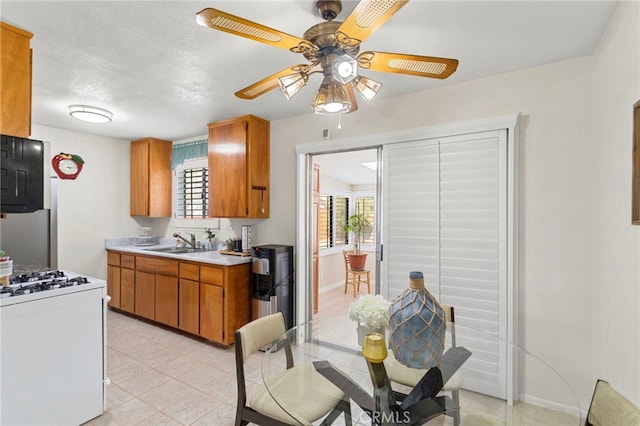 kitchen with ceiling fan, white range with gas stovetop, brown cabinetry, and a sink