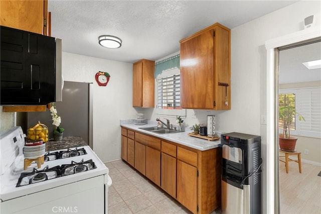 kitchen featuring baseboards, white range with gas cooktop, a sink, light countertops, and brown cabinets