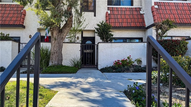 doorway to property with stucco siding, fence, and a tiled roof