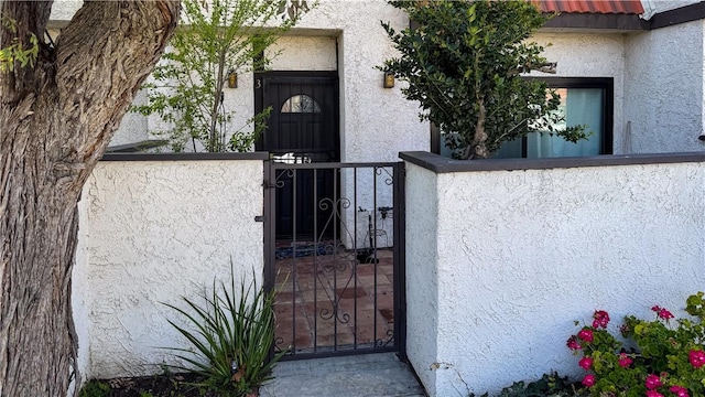 doorway to property with a gate, fence, and stucco siding