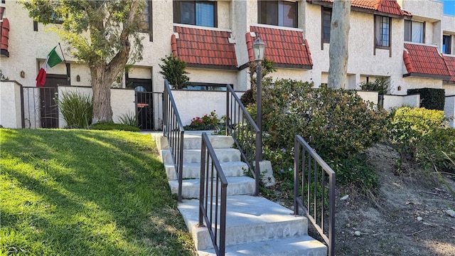 exterior space with stucco siding, stairway, a front yard, and a tile roof