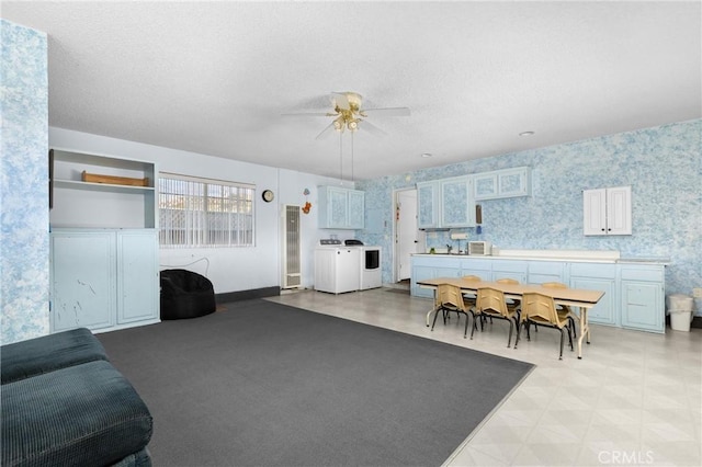 living area with wallpapered walls, ceiling fan, light floors, washer and dryer, and a textured ceiling