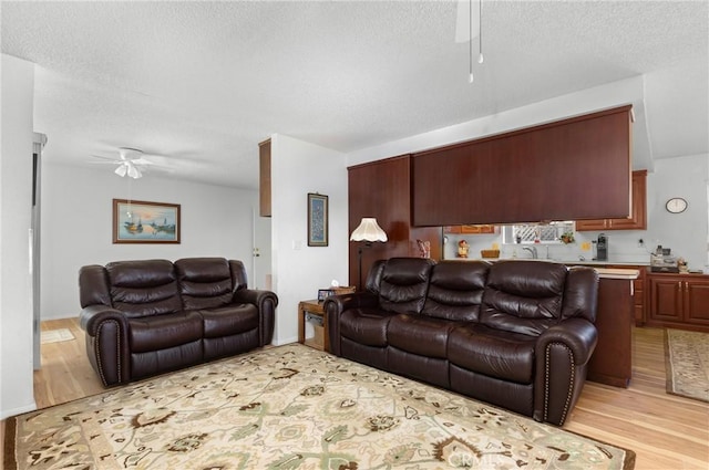 living room with light wood-style flooring, a ceiling fan, and a textured ceiling