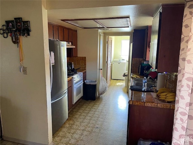 kitchen featuring under cabinet range hood, light floors, washer / dryer, freestanding refrigerator, and white electric range oven