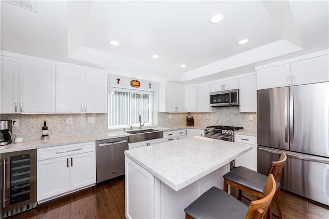 kitchen with wine cooler, appliances with stainless steel finishes, a raised ceiling, and a sink