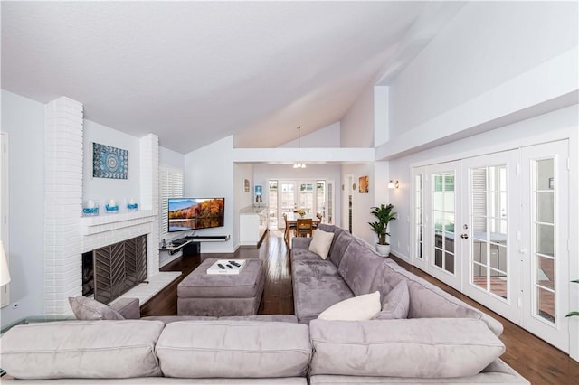 living area featuring vaulted ceiling, a healthy amount of sunlight, a brick fireplace, and wood finished floors