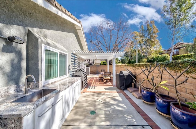 view of patio featuring exterior kitchen, a fenced backyard, a pergola, a sink, and a grill