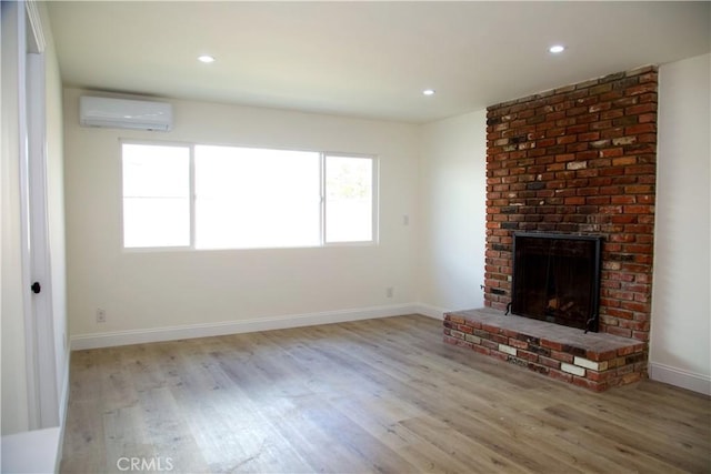 unfurnished living room featuring a wall mounted AC, wood finished floors, recessed lighting, baseboards, and a brick fireplace