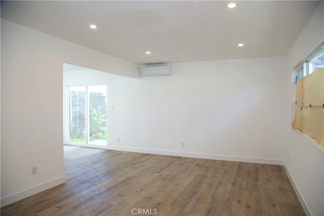 empty room featuring an AC wall unit, recessed lighting, wood finished floors, and baseboards