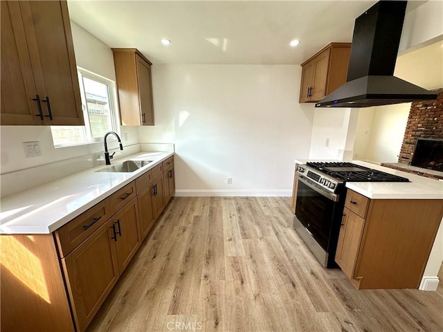 kitchen with light wood finished floors, island exhaust hood, stainless steel range with gas cooktop, and a sink