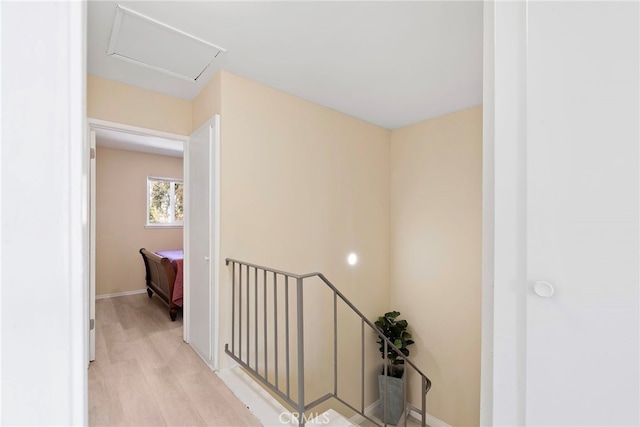 corridor featuring an upstairs landing, baseboards, and light wood finished floors