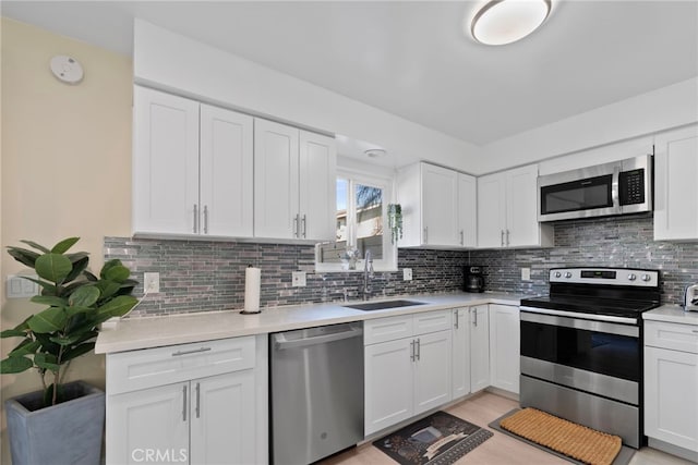 kitchen featuring a sink, stainless steel appliances, white cabinets, light countertops, and decorative backsplash