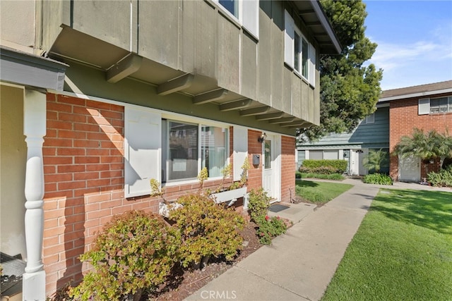 view of exterior entry with brick siding and a lawn