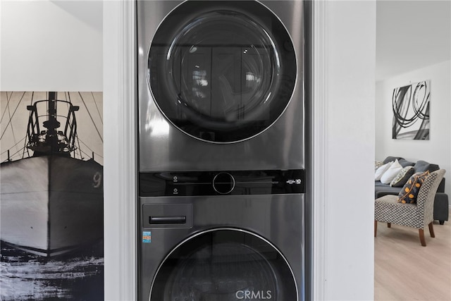 clothes washing area with wood finished floors, laundry area, and stacked washing maching and dryer