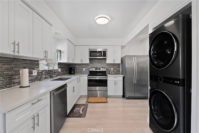 kitchen featuring a sink, stacked washer / dryer, white cabinets, and stainless steel appliances