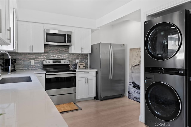 kitchen with white cabinets, stacked washer / drying machine, appliances with stainless steel finishes, and a sink