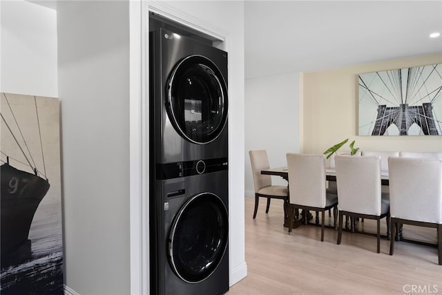 laundry area with laundry area, stacked washer and clothes dryer, baseboards, and wood finished floors