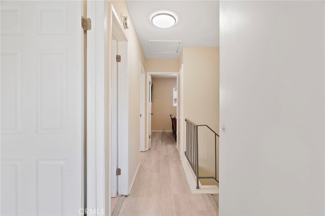 corridor featuring attic access, light wood-style flooring, and baseboards