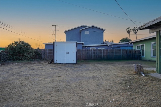 yard at dusk featuring an outbuilding, a storage shed, and fence