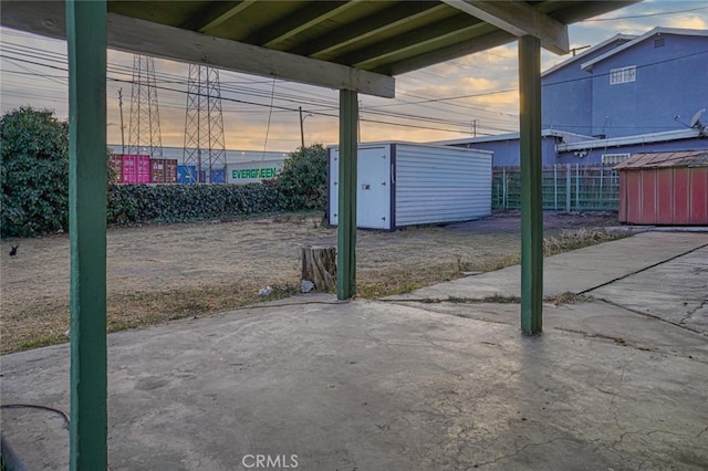 patio terrace at dusk featuring a storage shed, fence, and an outdoor structure