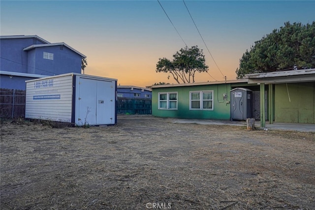 back of house at dusk featuring an outbuilding, a storage unit, and fence