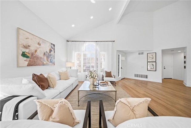 living area with high vaulted ceiling, wood finished floors, visible vents, and baseboards