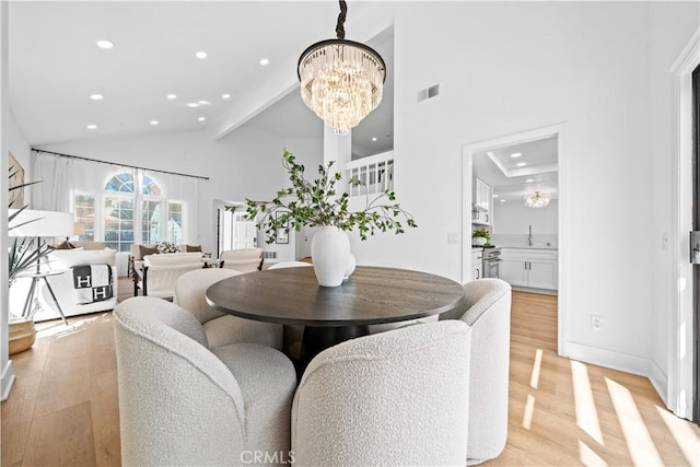 dining area with visible vents, high vaulted ceiling, light wood-type flooring, and an inviting chandelier