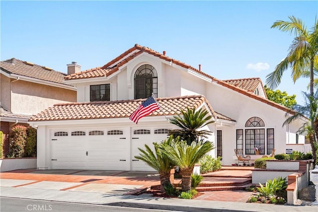 mediterranean / spanish house with a tiled roof, a garage, driveway, and stucco siding