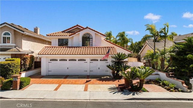 mediterranean / spanish house featuring a tiled roof, an attached garage, driveway, and stucco siding