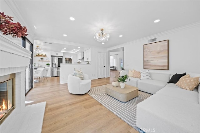 living room with visible vents, a notable chandelier, ornamental molding, a fireplace, and light wood finished floors