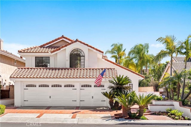 mediterranean / spanish home with stucco siding, a tiled roof, and an attached garage