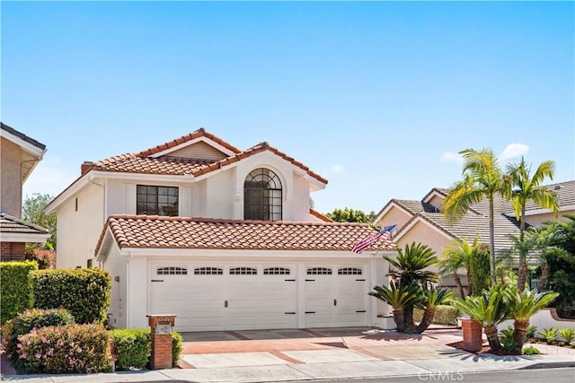 mediterranean / spanish house with a tile roof, concrete driveway, a garage, and stucco siding