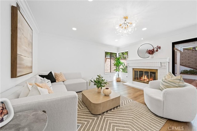 living area featuring a notable chandelier, wood finished floors, recessed lighting, a fireplace, and crown molding