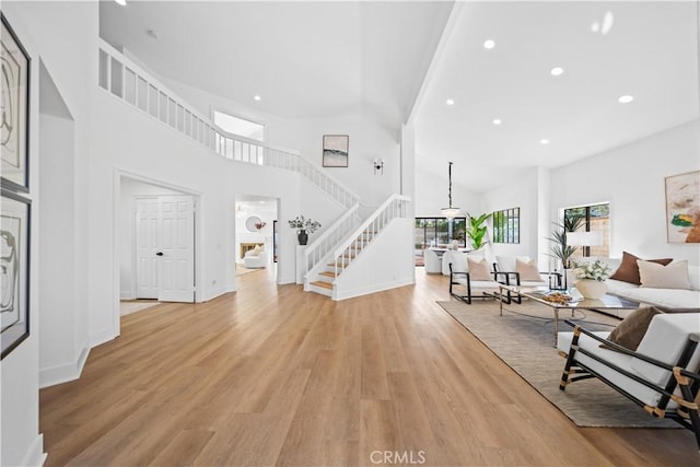 living area with high vaulted ceiling, light wood-style flooring, recessed lighting, stairway, and baseboards