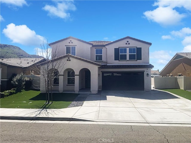 mediterranean / spanish-style home featuring stucco siding, driveway, fence, a front yard, and an attached garage