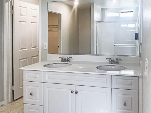 bathroom with a sink, a shower with shower door, and double vanity