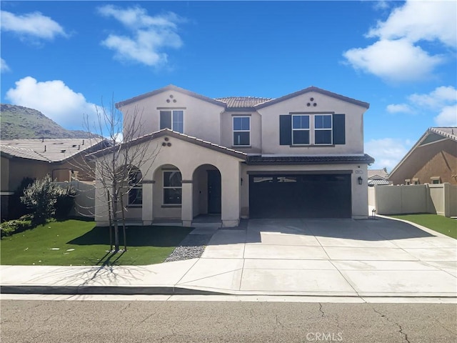 mediterranean / spanish-style home with stucco siding, driveway, fence, a front yard, and an attached garage