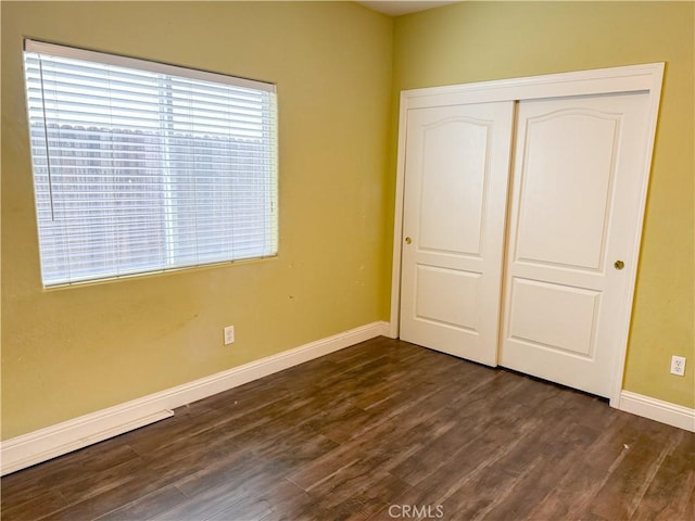 unfurnished bedroom featuring a closet, dark wood finished floors, baseboards, and multiple windows