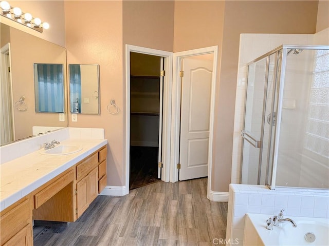 bathroom featuring a walk in closet, a stall shower, wood finished floors, a bath, and vanity