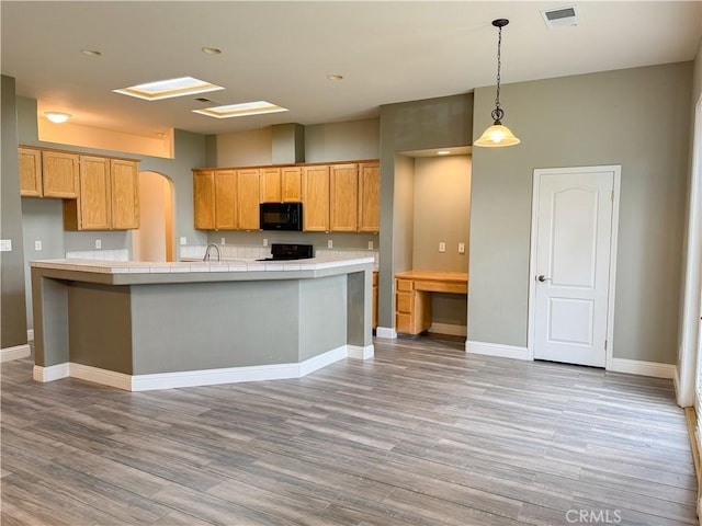 kitchen featuring light wood finished floors, visible vents, baseboards, black appliances, and a sink